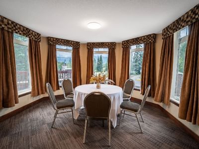 Well-lit dining area at Falcon Crest Lodge features a round table with chairs, surrounded by large windows