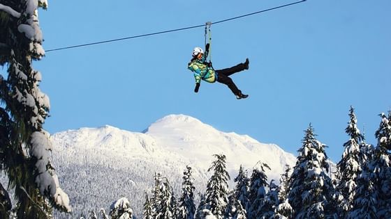 Person soaring on a zipline through the snowy mountains near Blackcomb Springs Suites