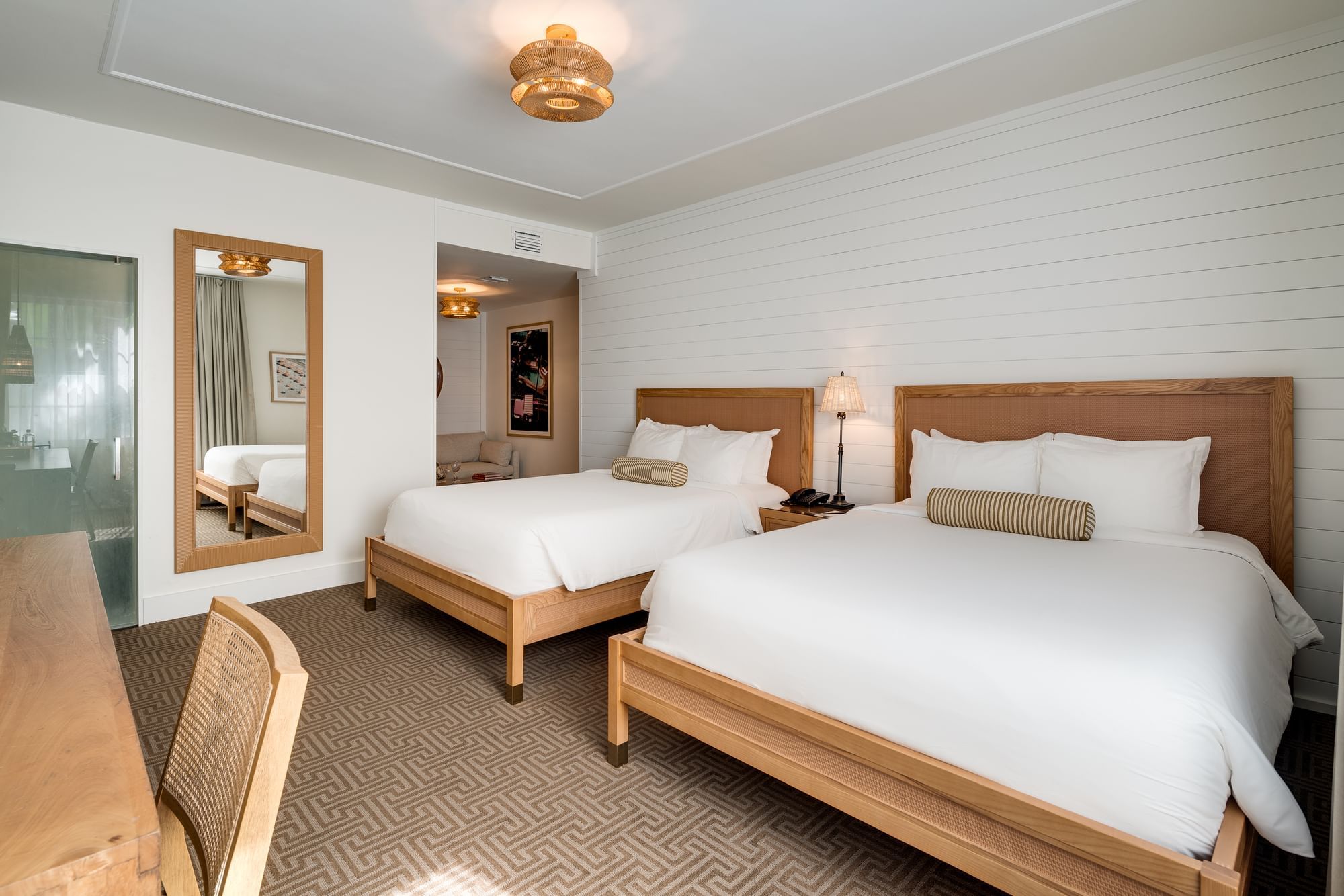 A hotel room with two beds, a desk, and a mirror.