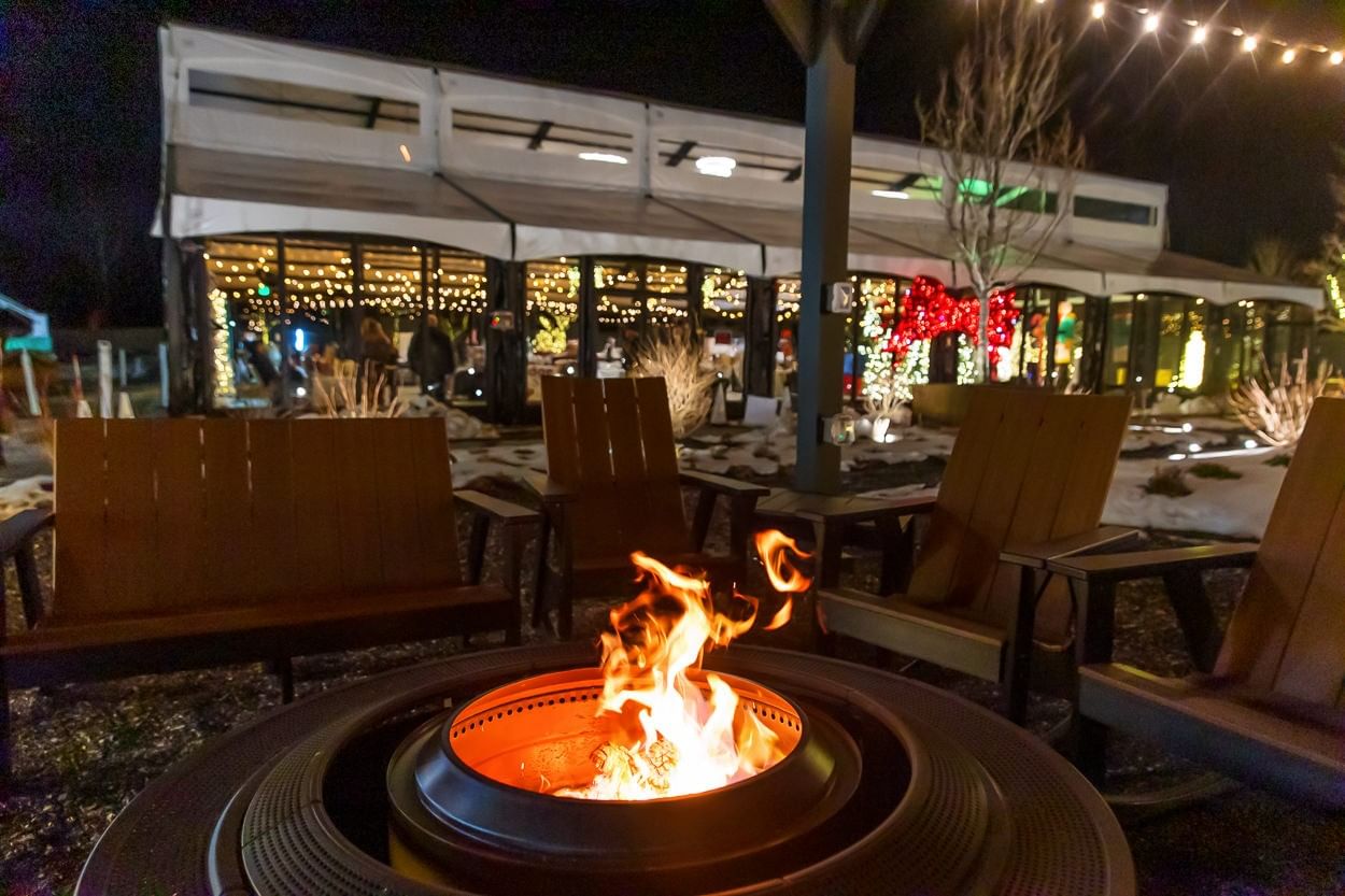 Warm fire pit surrounded by wooden seats outside decorated event hall in The Secret Garden Pergolas at The Brook
