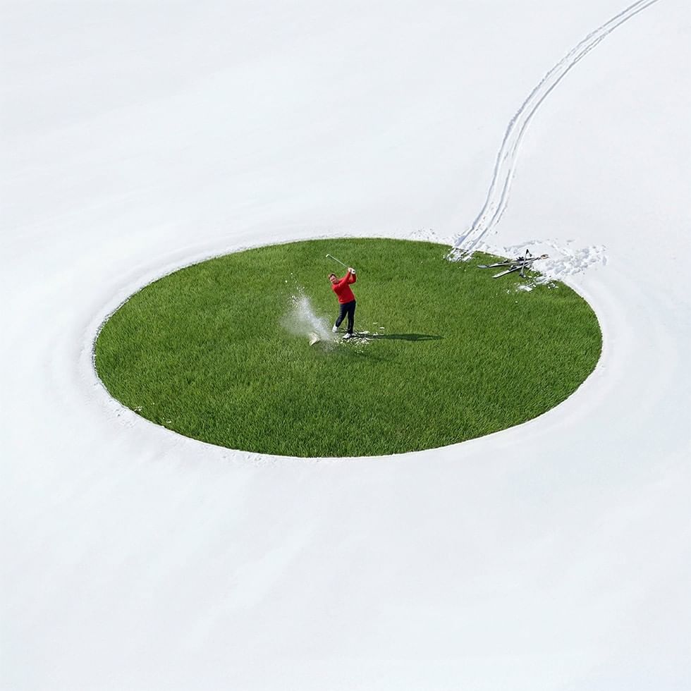 Golfspieler schwingt seinen Schläger auf einer schneebedeckten Wiese mit Skiern.