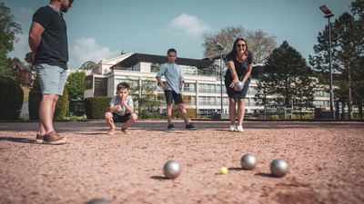 A family of four plays boules on a gravel surface with a building and trees behind.
