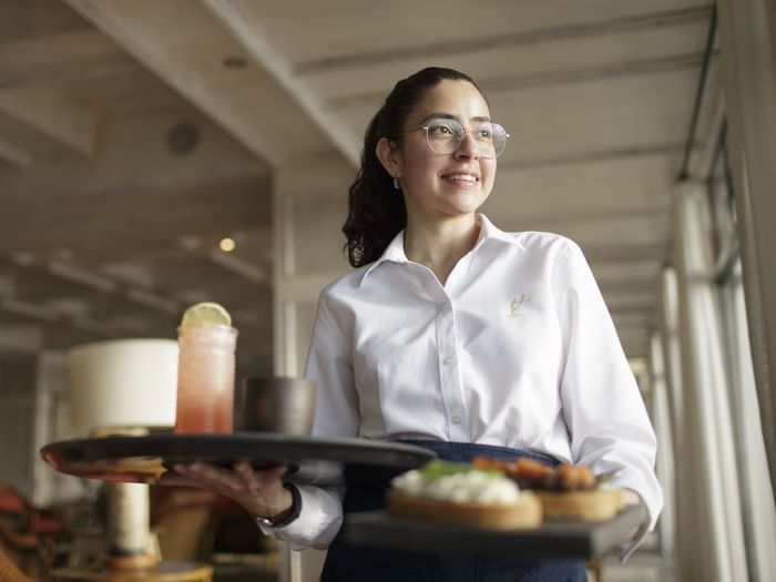 Waitress holding trays with meals & drinks at Hoteles Australis