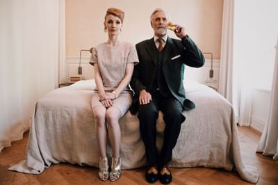 Elegant woman in sparkling dress sitting by an older man holding a banana with a soft background at Hotel Motto Vienna