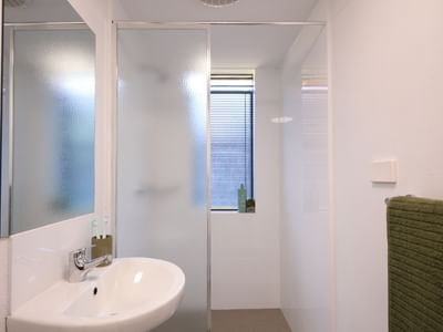 White bathroom with sink, mirror, glass shower enclosure, and green towel at UniLodge at Curtin University - Erica Underwood House.