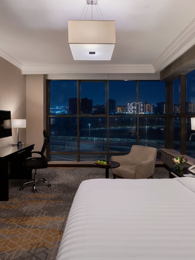 Wall-mounted TV, work desk, and cozy lounge chair by the beds in the Superior Room with city views at Warwick Hotel Jeddah