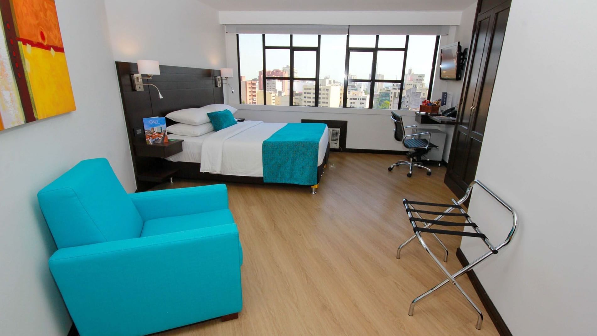 Habitación Dann Cali estándar con cama, almohadas, cuadros en la pared, ventana y decoración en tonos azul y gris en el hotel Dann Carlton Cali: la mejor opción de estadía en Cali.