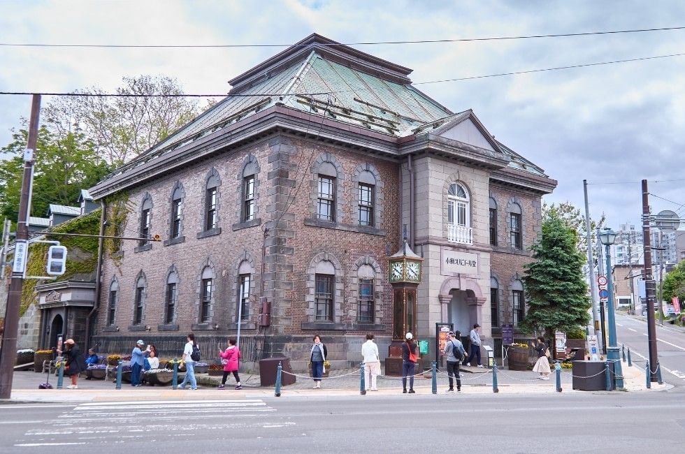Pedestrians outside historic brick building of Otaru Music Box Museum with steam clock near Grand Park Otaru