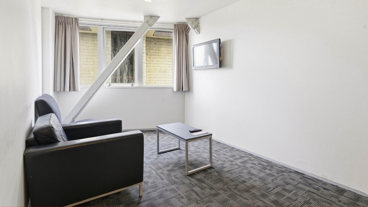 Small room with couch, coffee table, and wall-mounted TV at Student Living Auckland Anzac.