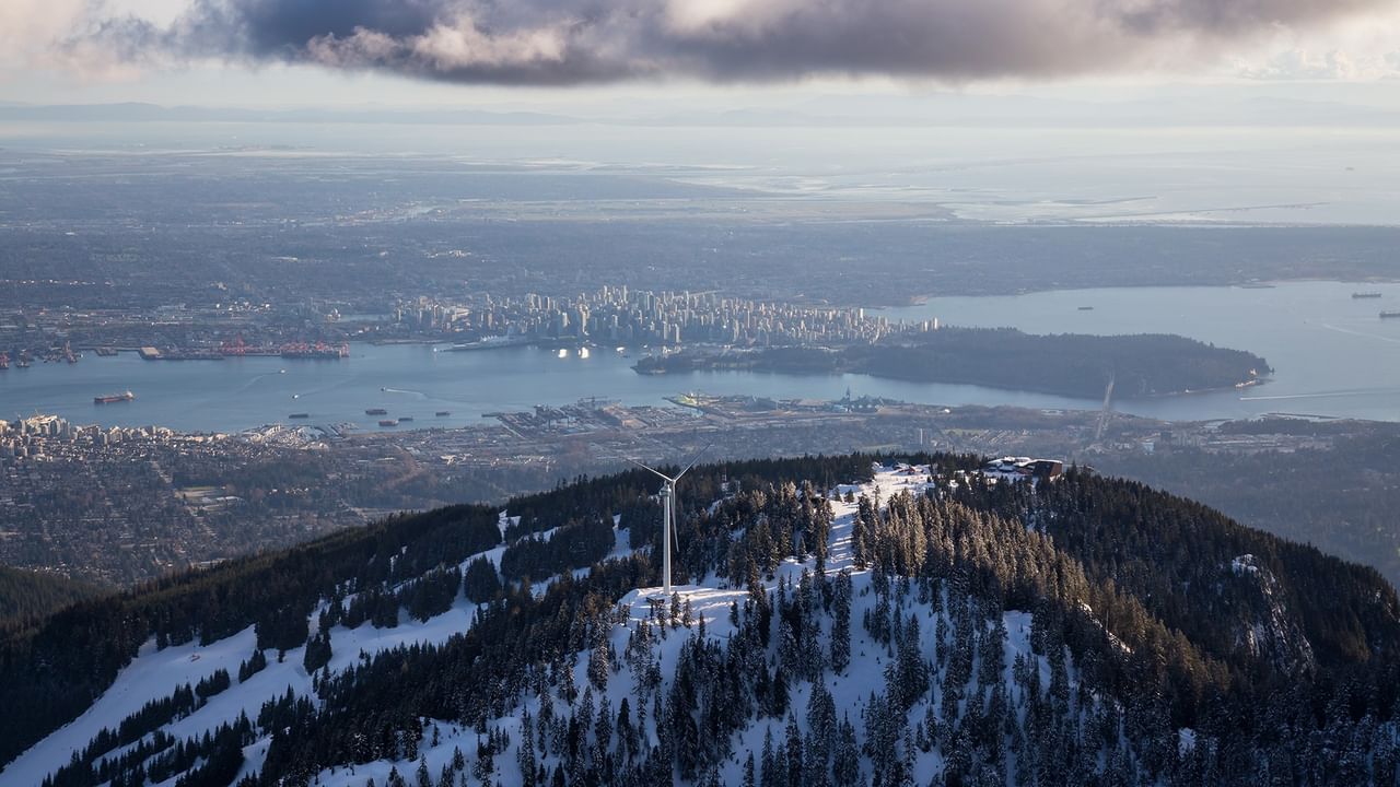 Aerial view of Vancouver, British Columbia, with a wind turbine on a snowy mountain peak near Coast Lonsdale Quay Hotel 