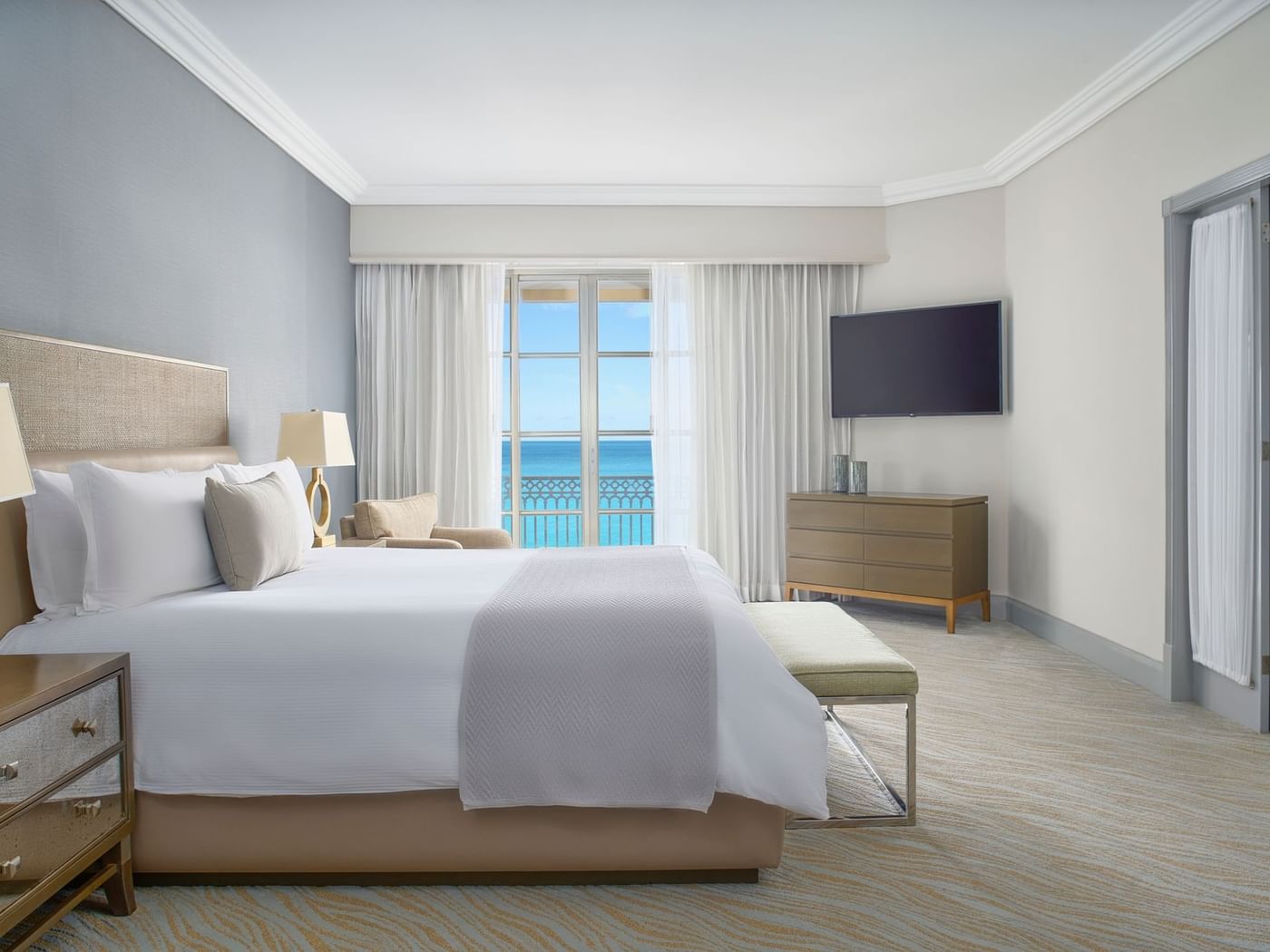 King bed, TV & cozy chair in Seafront Suite with carpeted floors at Kempinski Hotel Cancún