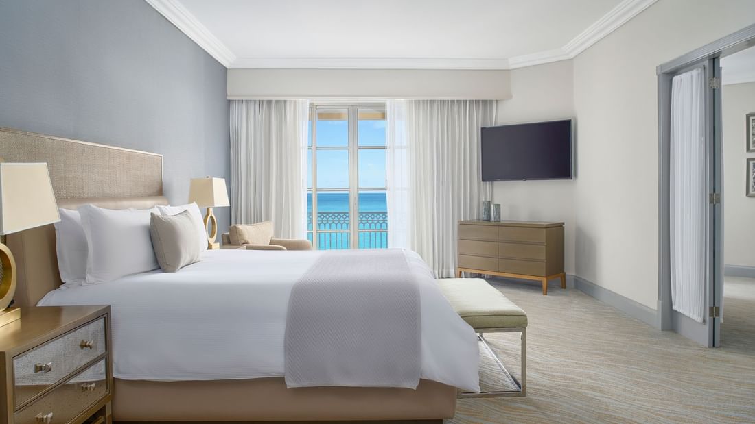 King bed, TV & cozy chair in Seafront Suite with carpeted floors at Kempinski Hotel Cancún