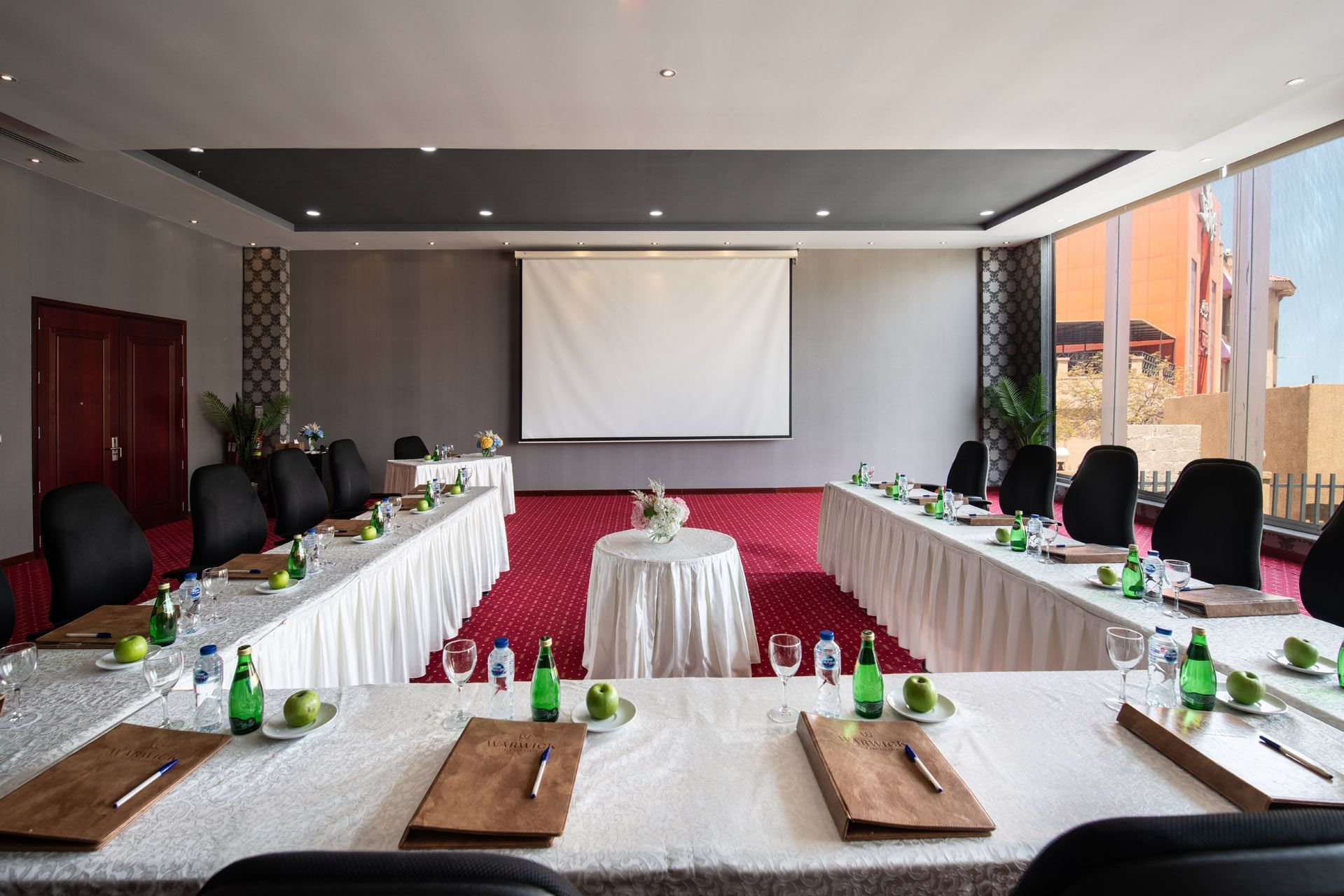 Amarige 3 conference room featuring tables set with water bottles, apples, and notepads, at Warwick Hotels and Resorts