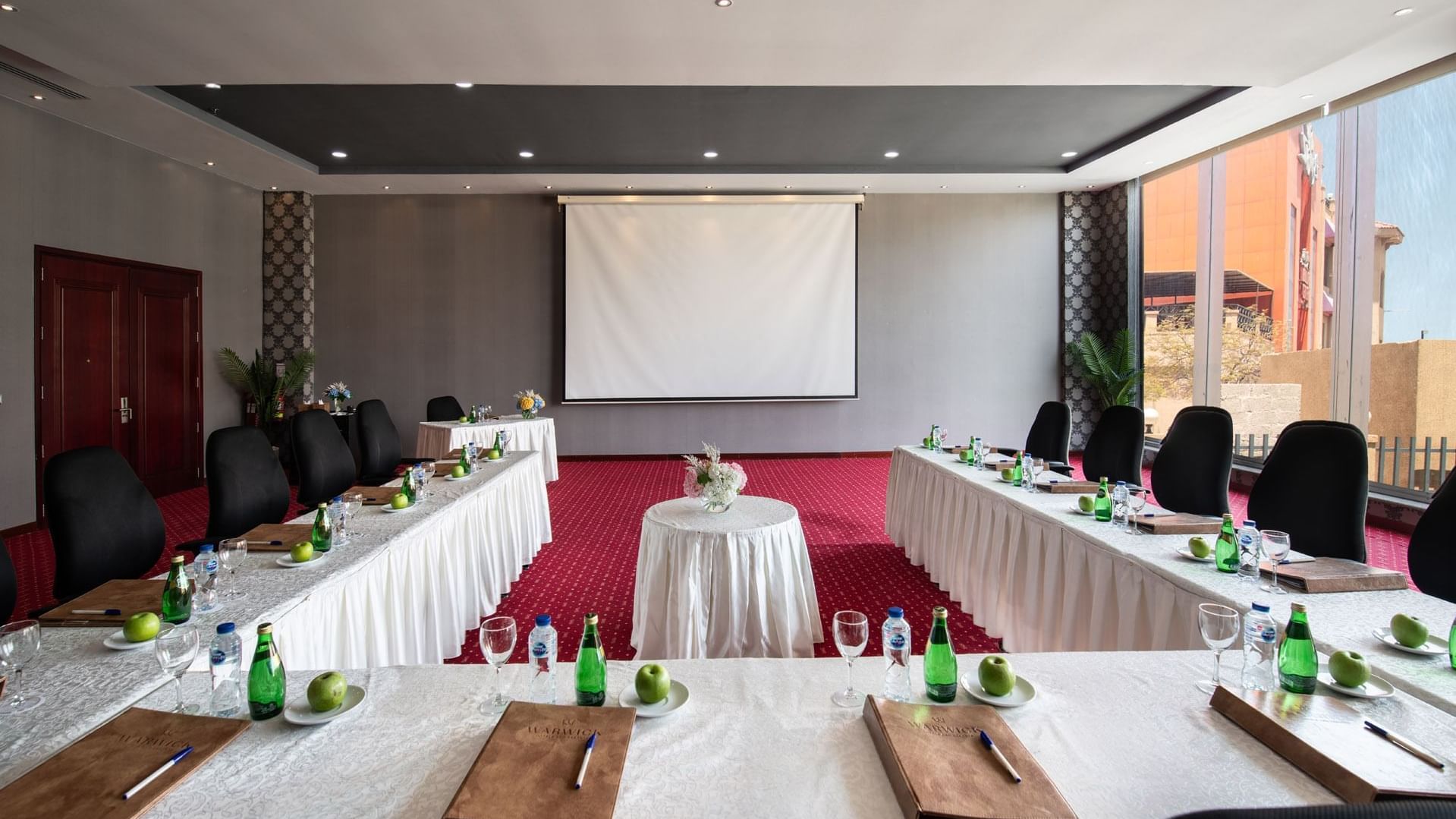 Amarige 3 conference room featuring tables set with water bottles, apples, and notepads, at Warwick Hotels and Resorts