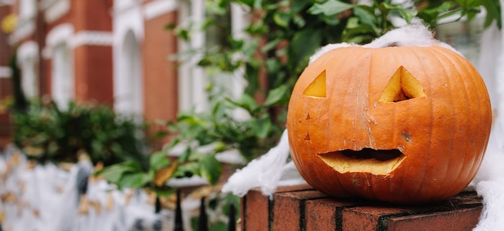 Carved jack-o’-lantern with triangular eyes and a smiling mouth sits outdoors on a stone surface