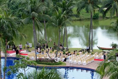 Outdoor wedding by a peaceful lake with decorated chairs and palm trees at The Saujana Hotel Kuala Lumpur