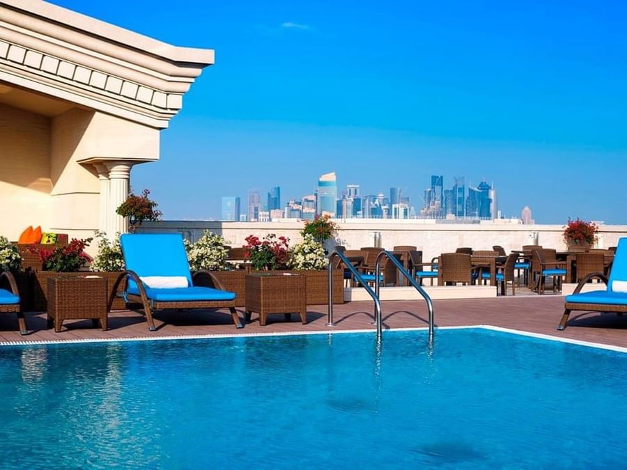 Blue pool loungers by a sparkling swimming pool under a clear blue sky at Warwick Doha Hotel