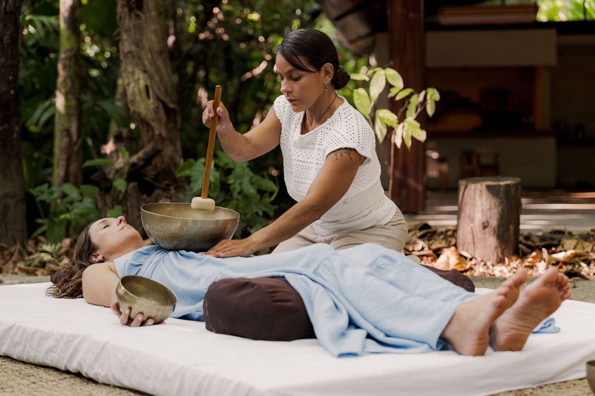 A woman is receiving a sound therapy session by a therapist at Cala Luna Boutique Hotel.
