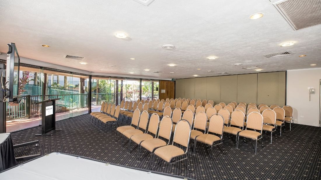 Theatre style table setup with podium, and large windows with a greenery view in Eacham Room at Mercure Hotel Townsville