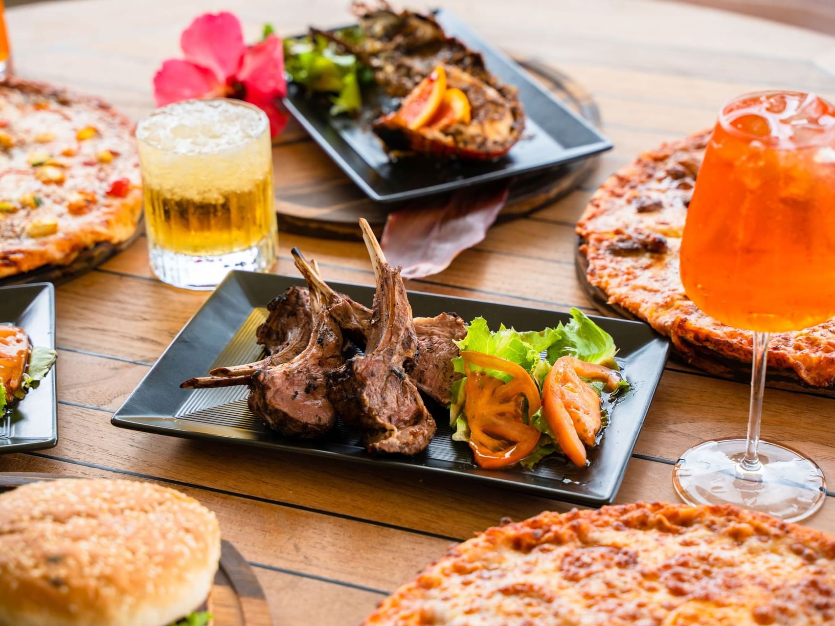 Tafel vol met lamskoteletten, twee pizza’s en drankjes in Bobbie’s Beach Club bij Golden Rock Resort