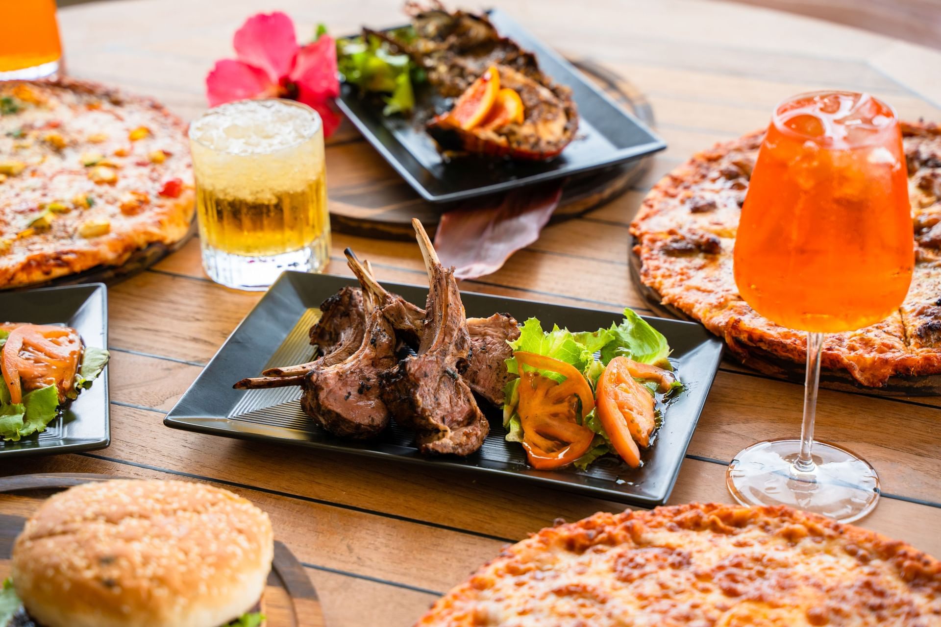Gedekte tafel met lamskoteletten, twee pizza’s en drankjes bij Bobbie's Beach Club in Golden Rock Resort