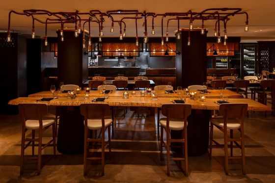 May Fair Kitchen interior featuring a large wooden table with stools under industrial lighting at The Kitchens