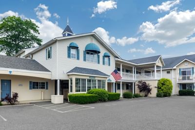 Charming Ogunquit Hotel and Suites with an American flag and lush greenery under a bright sky with fluffy clouds