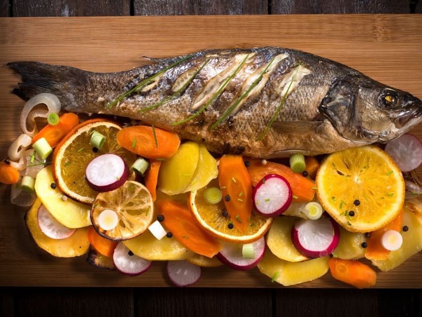 Exquisito pescado a la parrilla servido con rodajas de cítricos y verduras asadas en Camino Real Hotels