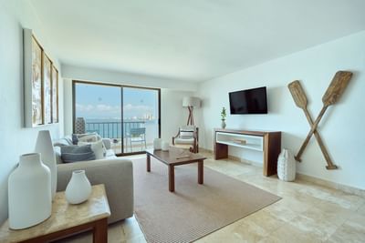 Living room with sofa, coffee table, TV, balcony, ocean view, and decorative elements.