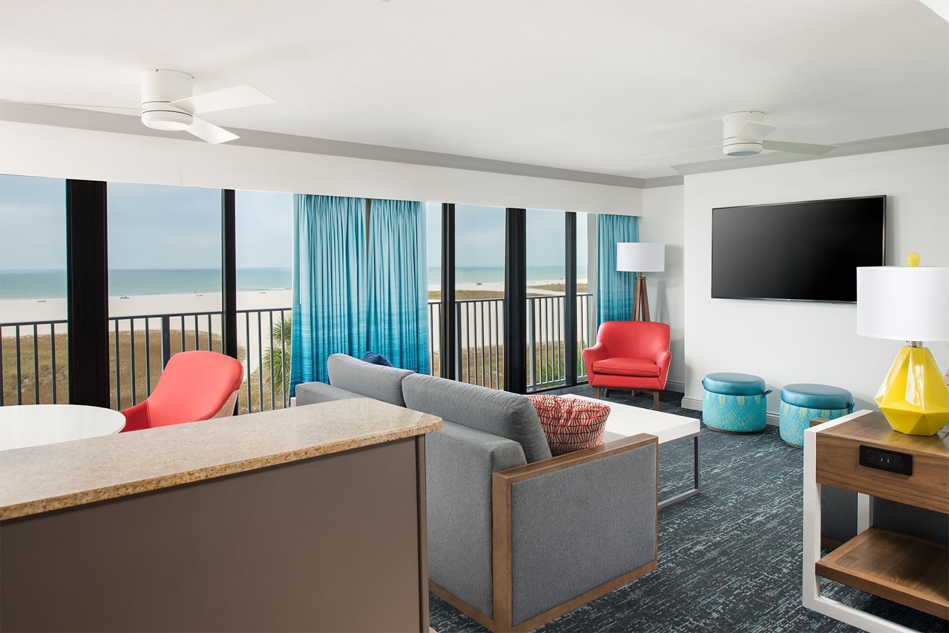 A wide view of a hotel suite living room with a sofa, chairs, TV, and balcony with ocean view.