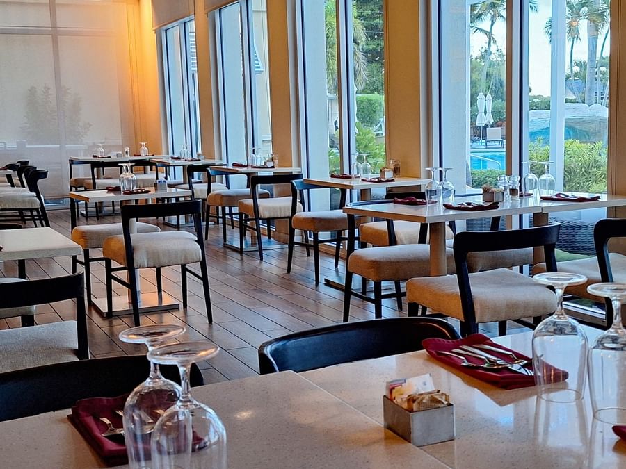 Verandah restaurant interior with Tables & glasses by padded chairs under soft light at Warwick Paradise Island Bahamas