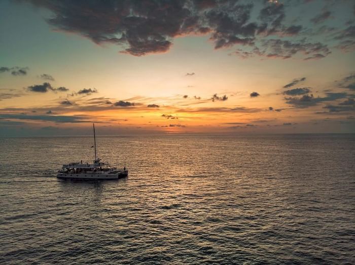 Sailing boat navigating across calm ocean waters under sunset sky with scattered clouds near Los Altos Resort