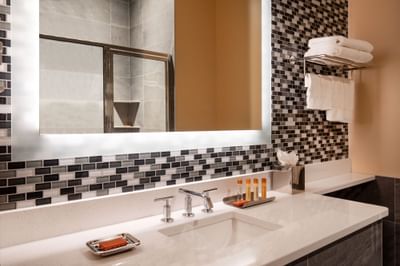 Bathroom vanity with a lighted mirror, mosaic tile backsplash and rolled towels at Harborside Inn Boston