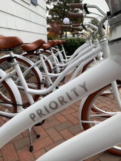 Row of Priority white bicycles with brown seats parking on a brick pathway at Breezeway Boutique Hotel