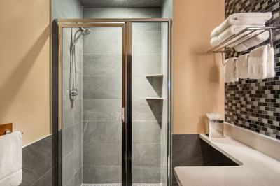 Bathroom featuring a walk-in glass shower stall next to a vanity with rolled towels on a rack at Harborside Inn Boston