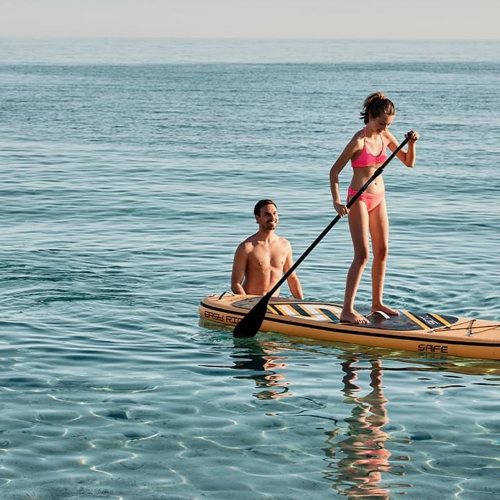 Due persone, una donna in bikini e un uomo, si godono una giornata di paddleboarding in mare.