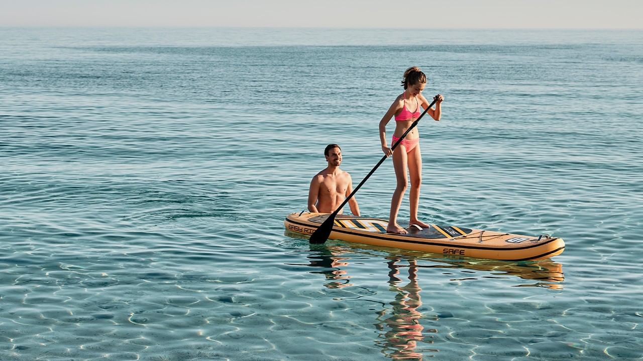 Two people on a yellow paddleboard in the ocean, one standing and one kneeling.