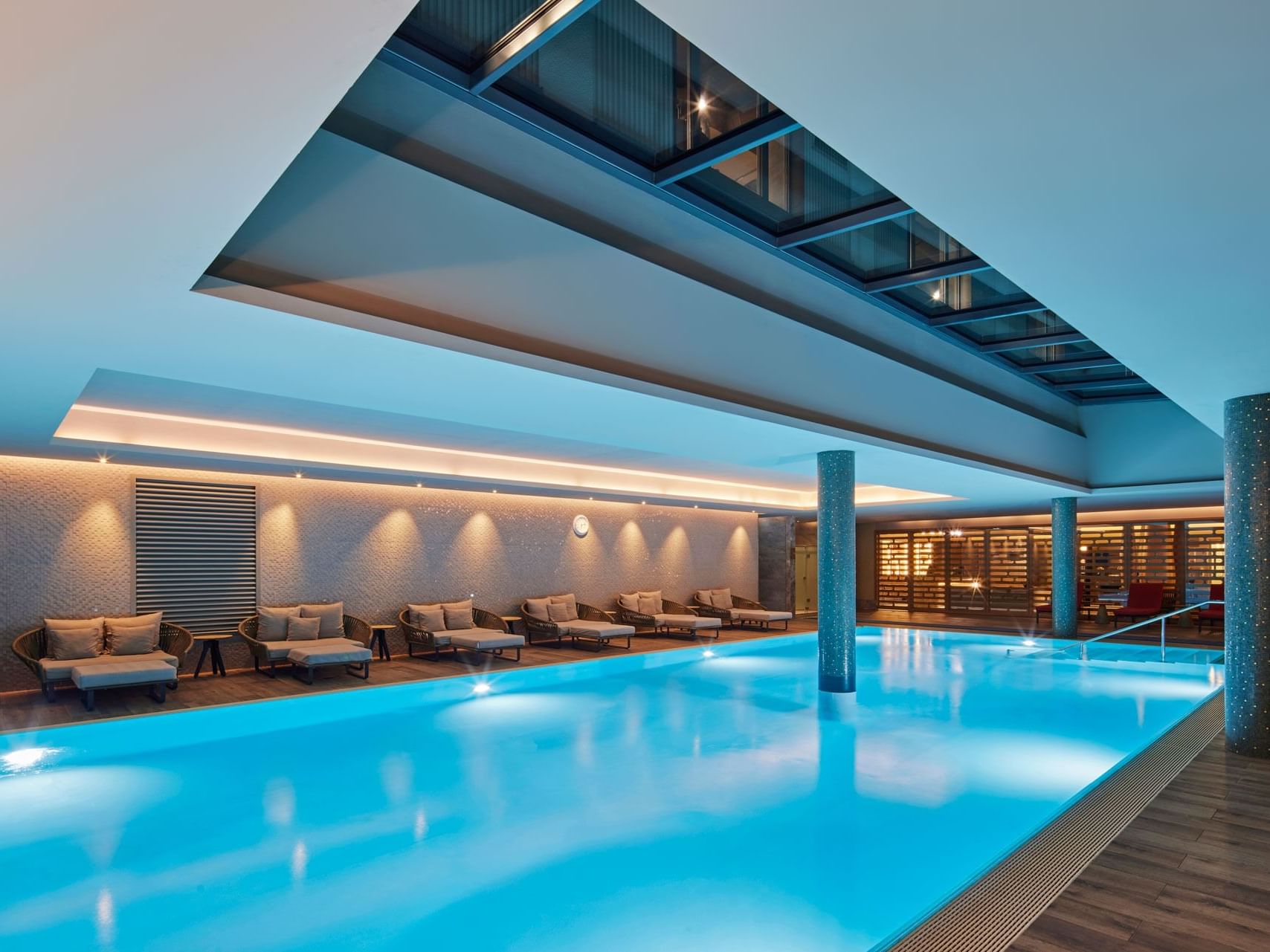 Elegantes Hallenbad mit Glasdach, Loungemöbeln und heller Beleuchtung – Titanic Chaussee Berlin.