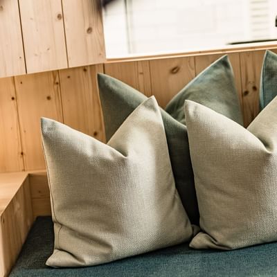 Gemütliche Sitzecke mit Kissen, Holzwand, Lampe, Brille und Buch auf einem Tisch.