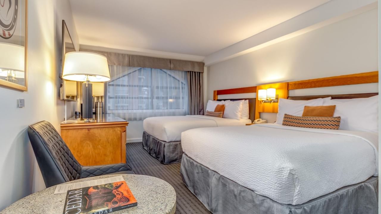 Two beds, a chair, and a table with a book in a hotel room.