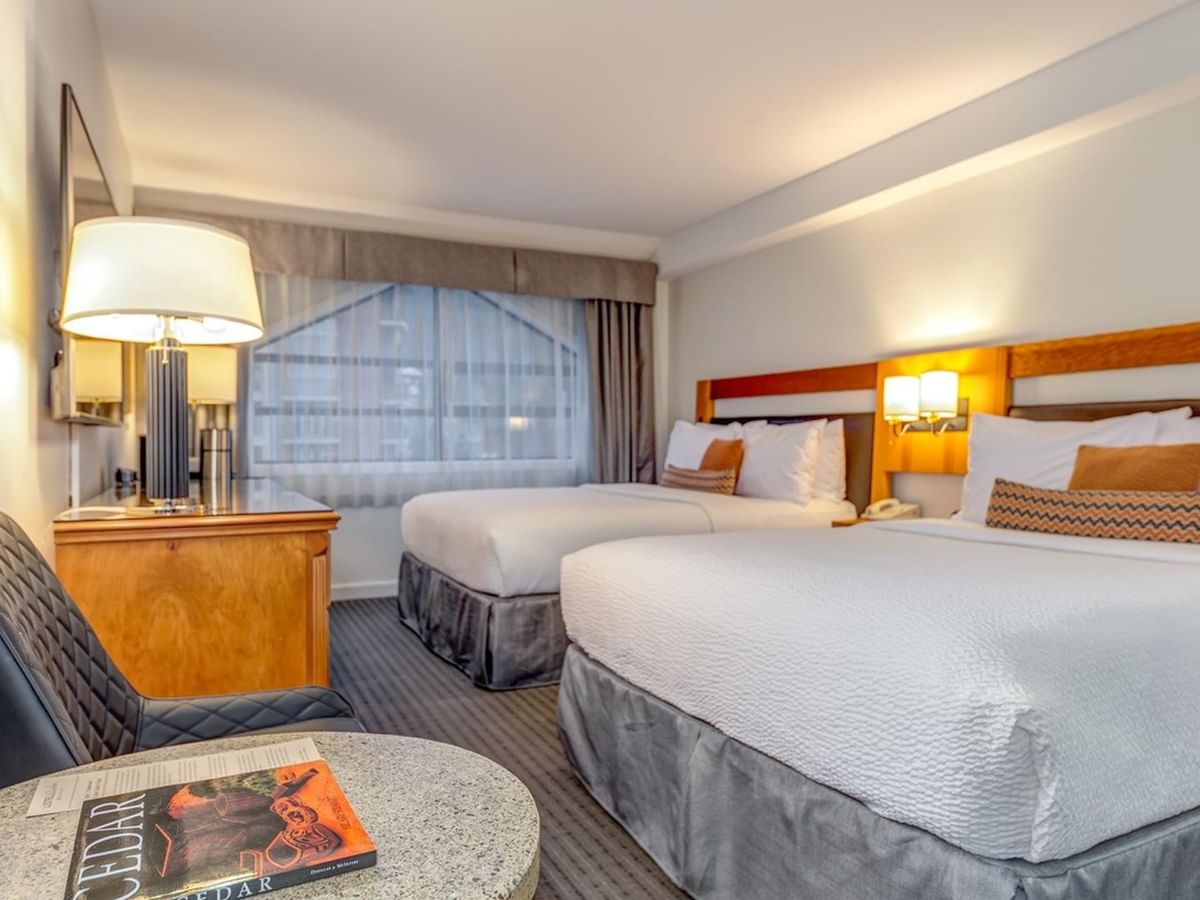 Hotel room with two beds, a chair, a table with a book, and a window.