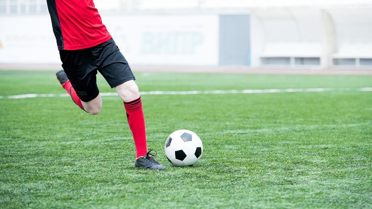 Soccer player kicking a ball on green field.