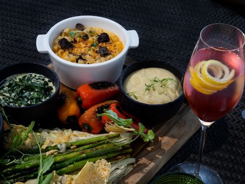 Plato de aperitivos con queso, espárragos y pimientos, acompañado de un coctel en De Cortez Grill House en Hacienda Del Mar Los Cabos.