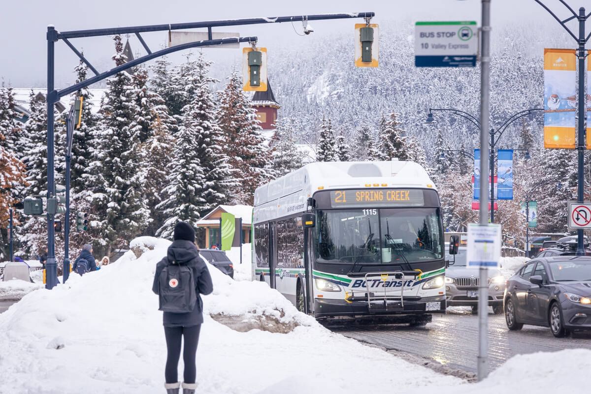 Woman waiting for public transport on snowy roadside near Blackcomb Springs Suites