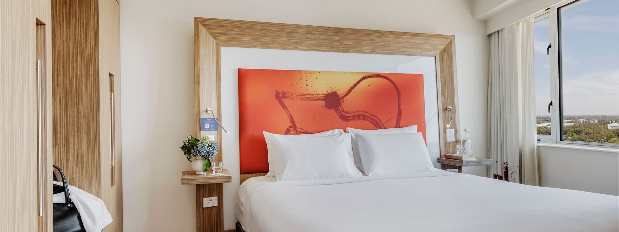 Plush king bed with cushioned headboard and vibrant orange artwork in Superior Spa Suites at Novotel Sydney Olympic Park