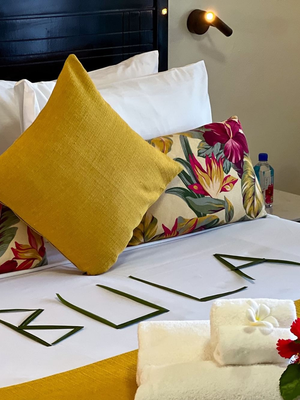 A neatly made bed with tropical-themed pillows and floral arrangement at Tokatoka Resort Nadi.