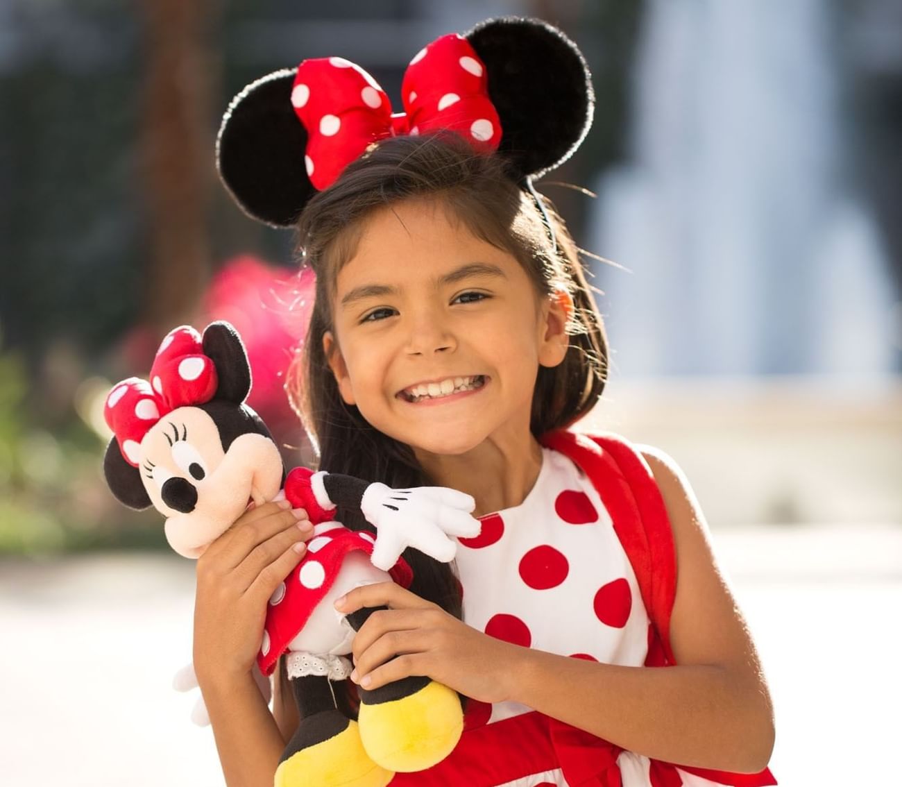 Child in a polka dot dress holding a Minnie Mouse plush toy in Walt Disney World near The Grove Resort & Water Park