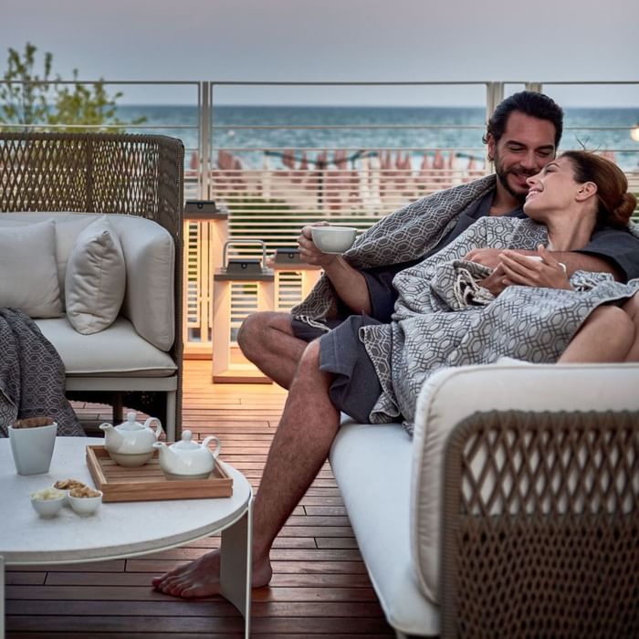 Couple relaxing on couch in outdoor balcony area with tea served on table at Falkensteiner Hotel & Spa Jesolo