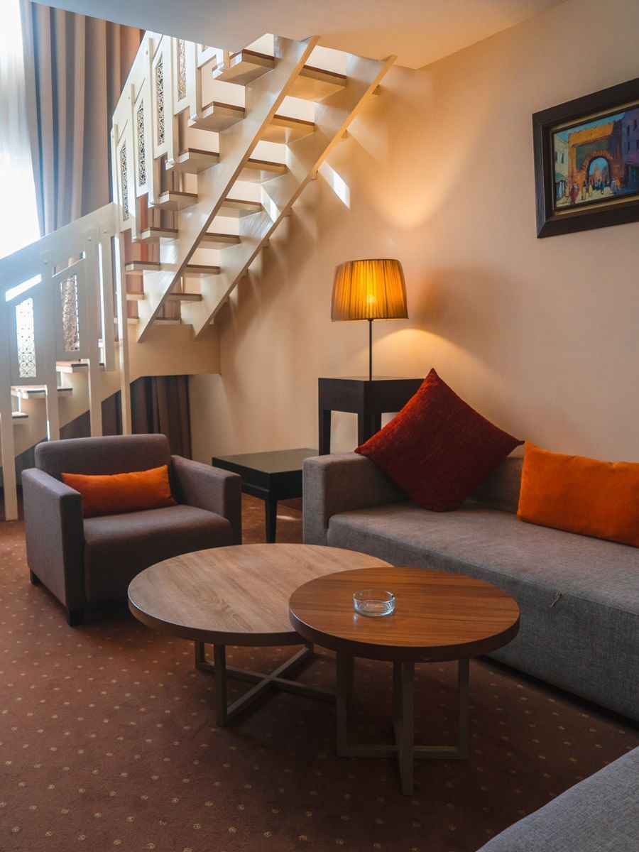 Salon élégant avec canapés, fauteuils, lampes, et escalier au Kenzi Basma