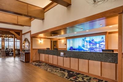 The front desk area of Lake Placid Club Grandview features a wood-paneled counter and a large illuminated scenic backdrop